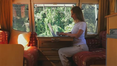 Jovem mulher trabalhando remotamente no laptop dentro da aconchegante van de campismo com