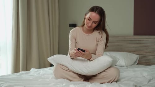 Woman Using Phone Sitting on Bed at Home