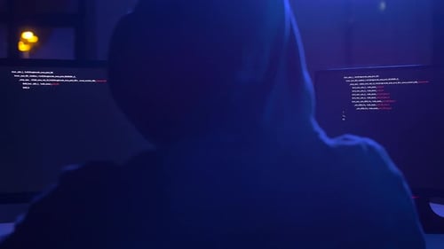 Hacker in Hood Working at Night on Computers