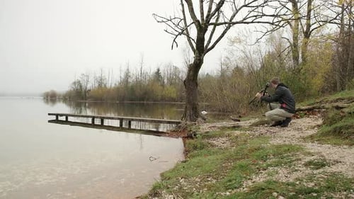 A photographer carrying photography equipment to set up to photograph next to a lake