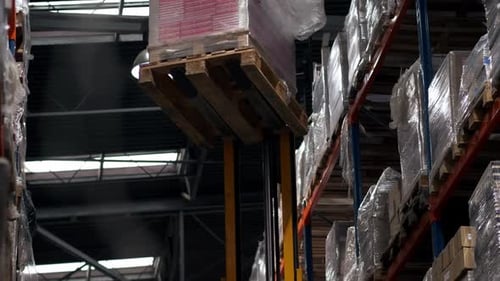 Load of goods on a pallet is picked up and moved by forklift inside warehouse