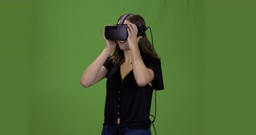 Young woman with a virtual reality head set on a green screen.