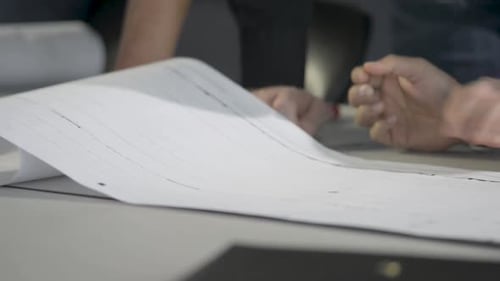 Hände arbeiten an architektonischen Plänen, Schwerpunkt Papier und Bewegung