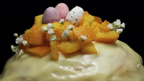 Osterkuchen mit Orange, kleinen Eiern und weißen Blumen auf schwarzem Hintergrund. Dreht sich in Nahaufnahme.