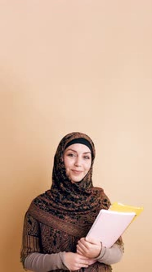 Junge lächelnde muslimische Studentin trägt Hijab und hält Bücher senkrecht