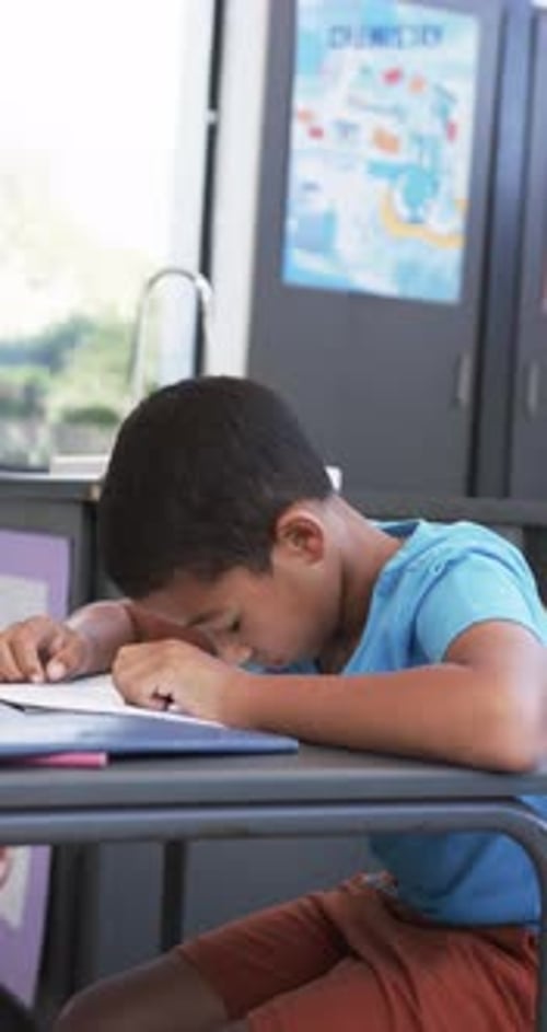 Vertical video: In school, boy resting head on desk, feeling tired in classroom
