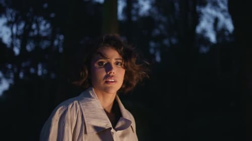 Garota em pé, floresta noturna iluminada por faróis de carro, closeup, mulher confusa