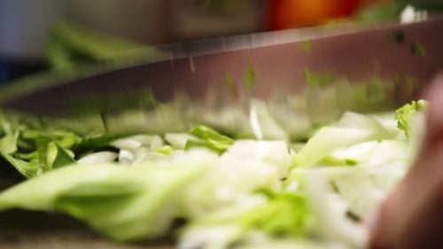Asian chef finely chopping leafy green vegetable with a sharp knife.