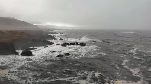 Luftaufnahmen über einem schwarzen Strand in Djupavogshreppur, Island. Harte Wellen treffen auf die Klippen in der
