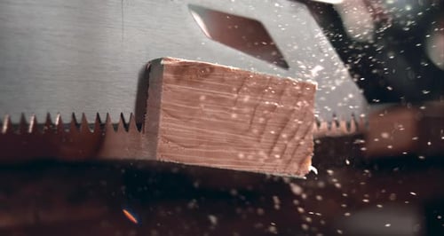 Saw cutting through wood, scattering fine dust particles in slow motion, detailed carpentry