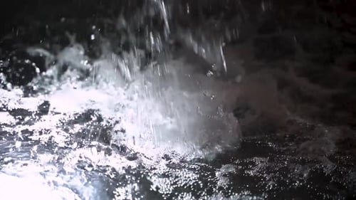 Stream of Water Splashing into Clear Illuminated Pool (Slow Motion)
