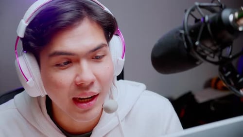 Young asian man for a podcast wearing headphones and speaking with mic in studio.