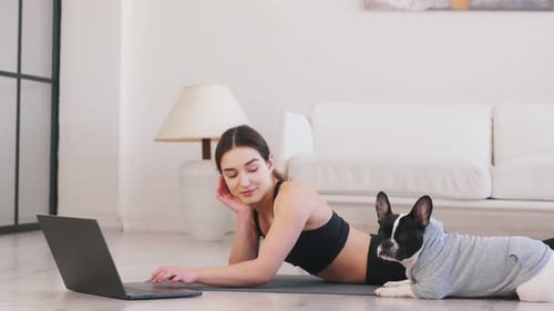 Searching the web on laptop. Woman with pug dog is doing yoga at home.