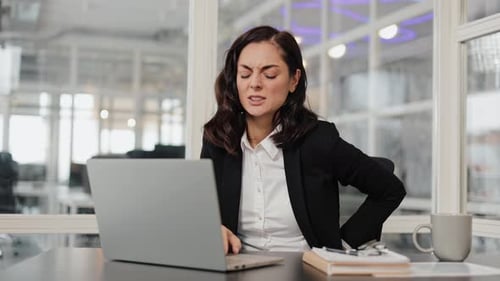 Business Woman Suffering From Back Pain in Office While Working on Laptop