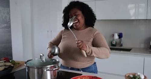 Feliz joven africana cocinando cantando y bailando en su cocina en casa
