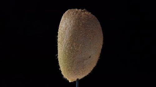 La mitad de un kiwi gira sobre un fondo negro,. primer plano