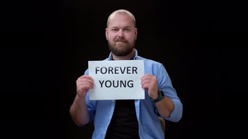 Glatzbärtiger Mann auf schwarzem Hintergrund zeigt die Inschrift FOREVER YOUNG auf Papier A Positive Guy