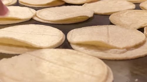 Corn tortillas on a flat griddle cooking, close-up shot, showcasing a golden and warm texture