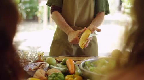 Man Peels Mango at Table with Fresh Vegetables