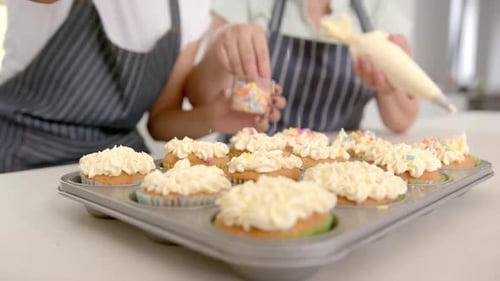 Cupcakes mit Streuseln verzieren, zwei Personen genießen Backaktivität zu Hause