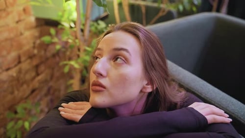 Dama con cabello rubio inclinado y mirando hacia arriba cerca de una pared de ladrillos y plantas