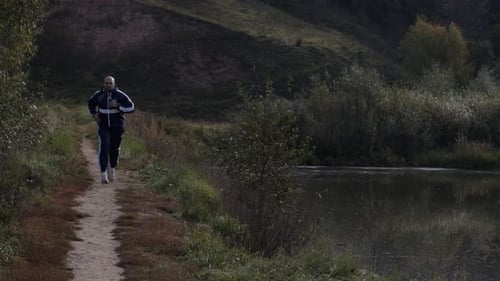 Sporty Adult Male Runner Jogging on Path Near Lake