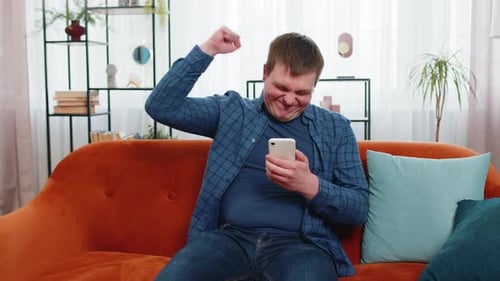 Man Celebrates Good News on Mobile Phone at Home
