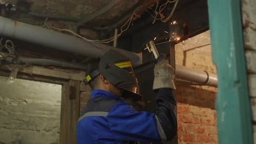Close Up Side Shot of Professional Welder in Safety Suit and Protective Mask Welds Metal Door Using