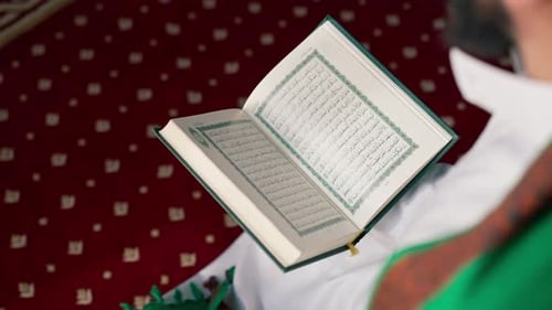 Nahaufnahme der Hände eines Muslims, der auf seinen Knien sitzt und in der Moschee mit dem Heiligen Koran betet