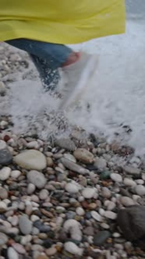 Vertical video. Female Legs in Sneakers and Jeans Running away from the Sea Wave, it catches up.