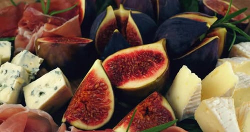 Des snacks sont servis sous forme de figues farcies au jambon et aux fromages bleus sur un plateau de service en pierre noire.
