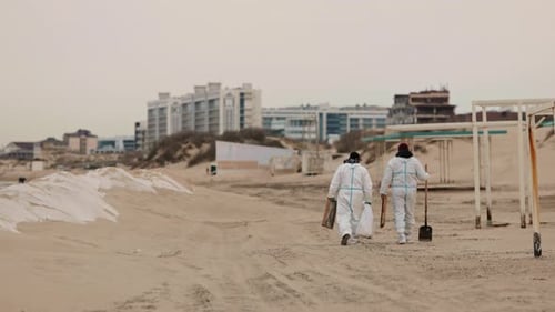 Workers in Suits Clean the Cloudy Beach