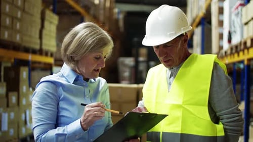 Senior Woman Manager Talking to Man Worker in a Warehouse
