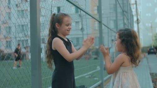 Duas lindas garotas caucasianas jogando palmas ao ar livre perto de um estádio de futebol, irmãs