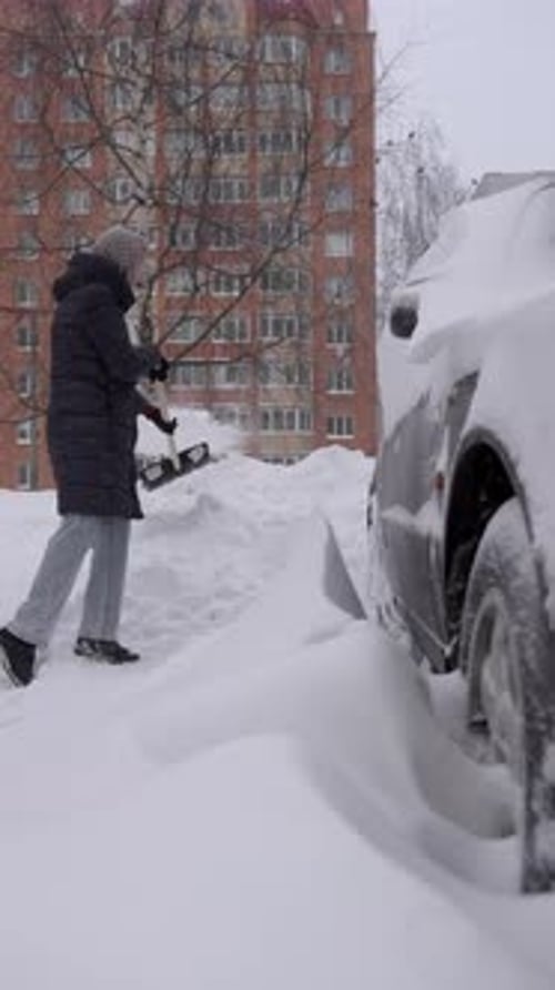 Woman shovels snow around car in winter