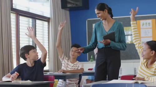 In school, teacher high-fiving student while another student writing in classroom