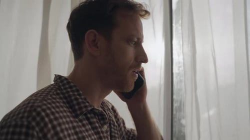 Man Angrily Talking on Phone Near Window