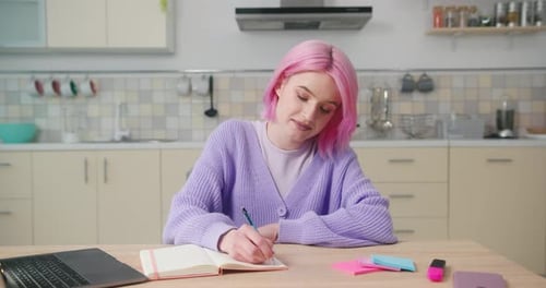 Woman With Pink Hair Writing in Notebook at Table