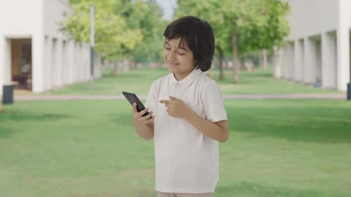 Happy Indian boy scrolling phone in park