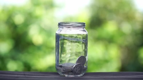 Putting money in glass jar against natural green background, saving concept