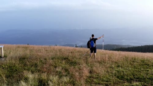 Male and female hikers with trekking poles point at the horizon and continue advancing along a mount