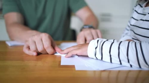 Child and Adult Folding White Paper at Table