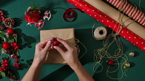 Decorating a Christmas Gift with Red Ornament and Twine on Green Background