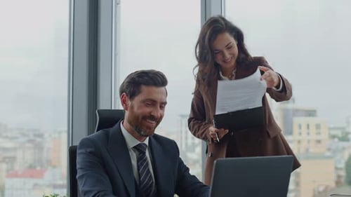 Lächelnder bärtiger Geschäftsmann, der mit einer attraktiven Sekretärin im Luxusbüro des Unternehmens zusammenarbeitet