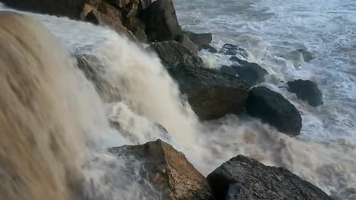 Strong current of water rushes over the rocks and falls into the sea