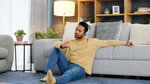 Happy relaxed man listening to music using headphones while sitting on the floor of his house