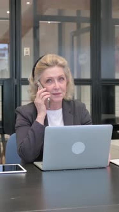 Professional Woman Answers Phone at Desk with Laptop