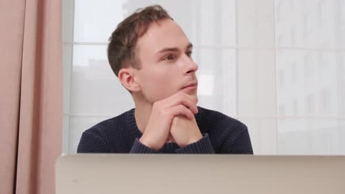 Young Adult Man Sitting and Thinking at Laptop