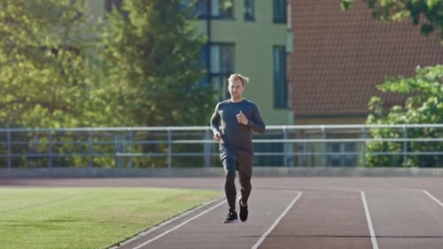 Smiling Athletic Fit Man in Grey Shirt and Shorts Jogging in the Stadium. He is Running Fast on a W