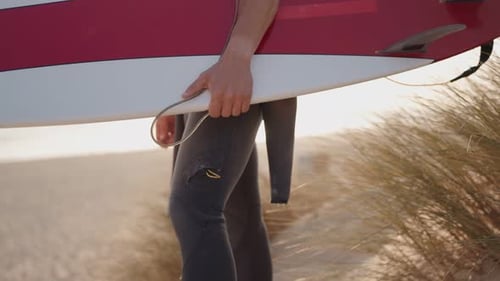 Surfer Walks Along Sandy Beach with Surfboard Towards Ocean Waves